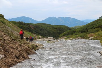 Fototapeta premium Tourists walks by mountain Tahkoloch river in the caldera of the extinct Vachkazhets volcano on the Kamchatka Peninsula, Russia.