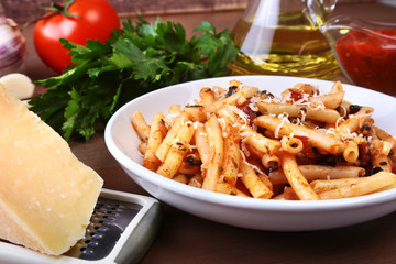 Spicy penne pasta bolognese with vegetables, chili and cheese in tomato sauce on the background of tomatoes, garlic, olive oil and spices.