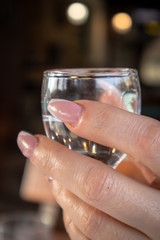 Women's hands holds small glass of alcohol drink in restaurant