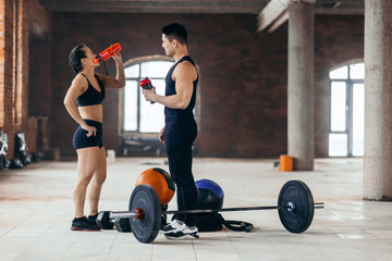 Fitness , cross fit. young strong man and woman drinking water during the training. copy space. full length side view photo.