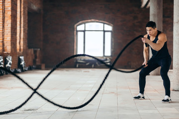 powerful guy using ropes during cross fit workout. free time. spare time, full length side view photo. copy space