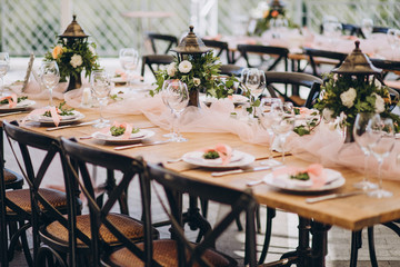 plates and glasses stand on the festive table, the table is decorated with flower compositions and cloth