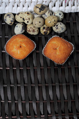 Quail eggs lie on the surface of a wicker vine. Nearby are cupcakes.