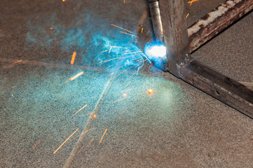 An experienced man performs work with a welding machine by fastening metal parts in an industrial production workshop.