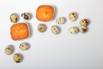 Quail eggs lie on the white surface. Nearby are cupcakes.  Next to the box with a gift wrapped in wrapping paper and tied with a ribbon.