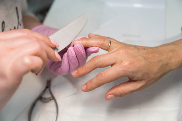 Obraz premium Nail care and manicure. Closeup woman in a beauty salon receiving a manicure by a beautician master. Manicurist hand painting client's nails. 