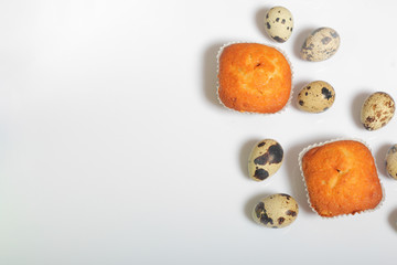 Quail eggs lie on the white surface. Nearby are cupcakes.  Next to the box with a gift wrapped in wrapping paper and tied with a ribbon.