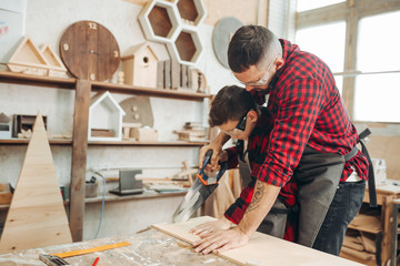 Experienced male teacher of carpentry skill acquaints a boy, with art of woodworking. Together with...
