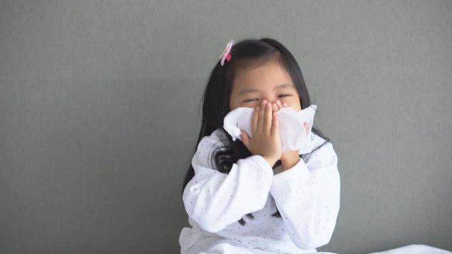 Asian child or kid girl sick with sneezing on nose and cold cough on tissue paper because weak or virus and bacteria from dust weather and kindergarten and pre school for medical background on 4K
