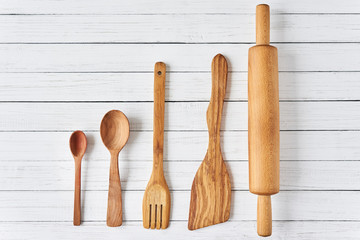 Wooden kitchen utensils on white wooden background with copy space. Spatula, spoons and rolling pin in row, top view