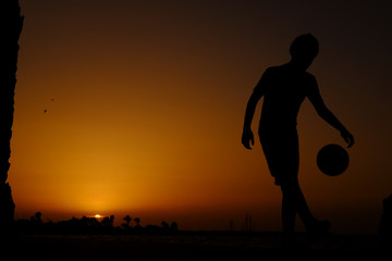 Boy playing football at sunset silhouette