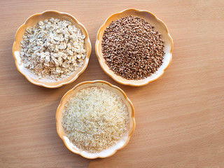 Polished rice, buckwheat groats and oatmeal are in saucers on the kitchen table.