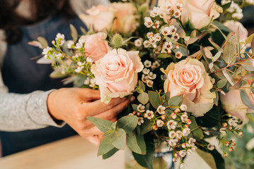 Woman florist makes a pink roses bouquet on wooden table