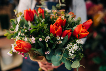 Woman florist makes a orange tulips bouquet on wooden table