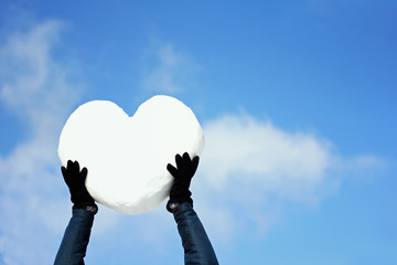 Men's hands with a big heart made of snow, on blue sky background. Declarations of love,...