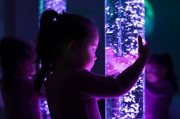 Child in therapy sensory stimulating room, snoezelen. Child interacting with colored lights bubble...