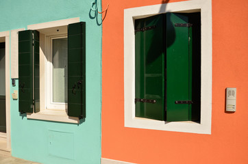 Colorful windows with shutters in Mediterranean style on orange and blue wall. Colorful houses in Burano island near Venice, Italy