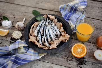 Fresh anchovies on plate with on a baking paper with a food around on the blue napkin