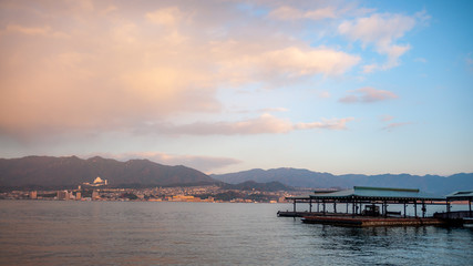 Landscape photo of the beautiful view that can be seen right outside the West Japan Railway Miyajima Ferry Terminal with the jetty in view, during the early morning, with dramatic clouds in the sky.