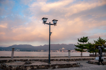 Photo of the beautiful view that can be seen right outside the Matsudai Kiden Miyajima Ferry Terminal during the early morning, with dramatic clouds in the sky and a vintage-looking lamppost.