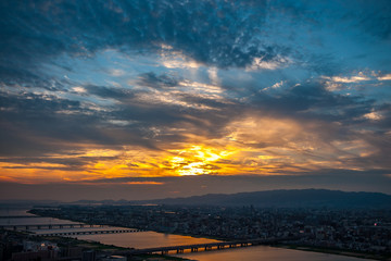 Panoramic, scenic view of Japan's Osaka city from the observatory deck of Umeda Sky Building during sunset with dramatic clouds in the blue and orange sky.