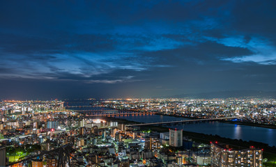Panoramic, scenic view of Japan's Osaka city from the observatory deck of Umeda Sky Building during sunset with dramatic clouds in the blue and orange sky.