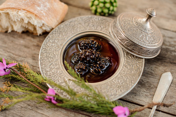 Delicious cones jam in the silver plate with a cap, tree branch and bread near it