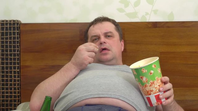 fan watches football on TV while lying on bed and scatters popcorn during a goal.