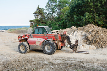 Red four wheel drive forklift tractor staying on a construction site.