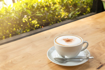 Side view of Hot cappuccino coffee in a white cup on the wooden table in a coffee shop and natural light background.