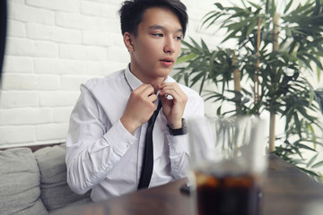 Fototapeta premium A young Asian businessman is waiting for a partner in a cafe. Business meeting in the restaurant. A Korean young man talking on the phone in a cafe.