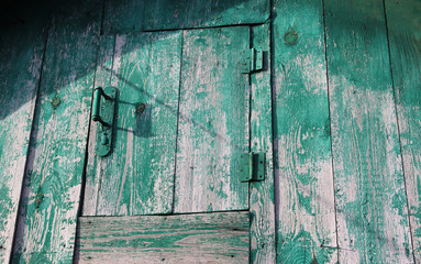 Wooden background. Several layers of aged, distressed paint. Green. Attic door with handle lock and hinges.
