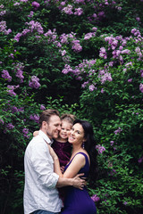 cheerful happy family hugging near lilac flowering bushes