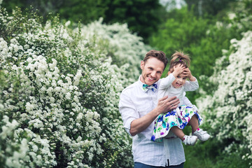 Cheerful dad and daughter are playing in nature among flowering spirea bushes