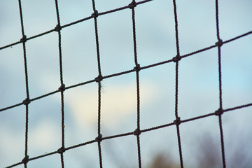 Square volleyball net made of rope against blue sky with clouds.