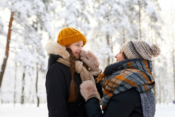 Side view portrait of happy mother tying scarf on cute little girl while having fun in winter forest, copy space