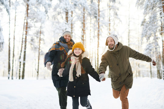 Portrait of playful family running in winter forest all smiling happily in sunlight, copy space