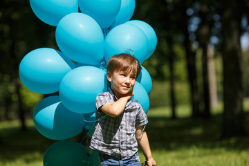 Fototapeta na wymiar A little boy runs in the park with a huge bunch of blue balloons.