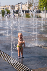 Smiling little boy on a hot summer day playing with a jet of water street fountain