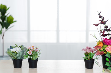 There are beautiful flowers and various objects in front of big living room windows.