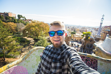 Travel and holidays concept - Happy guy making selfie portrait with smartphone in Park Guell, Barcelona, Spain.