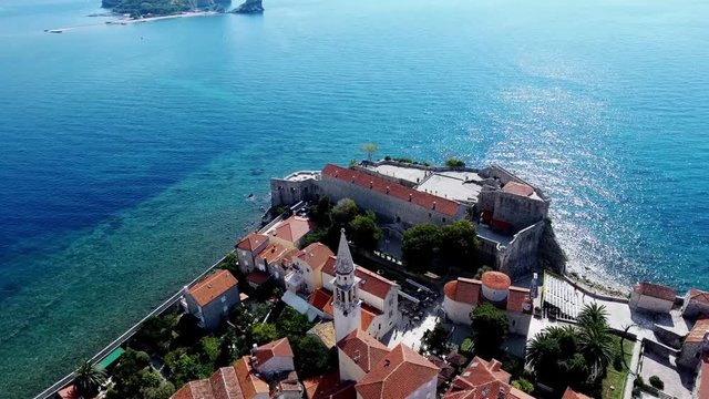 Budva with a bird's eye view. Becici. Drone takes pictures from a height. In the lens of the sea, sky, houses in the old style. Resort town with brown roofs.  Modern hotels by the sea. Port 