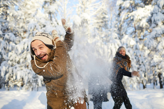 Portrait of happy family enjoying snowball fight in beautiful winter forest, focus on bearded man in foreground, copy space