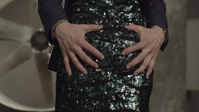 Close-up of male hands in formal wear grabbing female bouncy buttocks in night club. Confident man touching hard booty fit buttocks of elegant woman in stylish dress while flirting indoors.