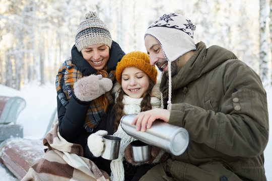 Portrait of happy family drinking hot tea in winter forest, copy space