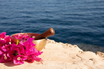 Tibetan singing bowl surrounded by pink tropical flowers. Tibetan bowl stands on a rock against the dark blue sea. Space for text.