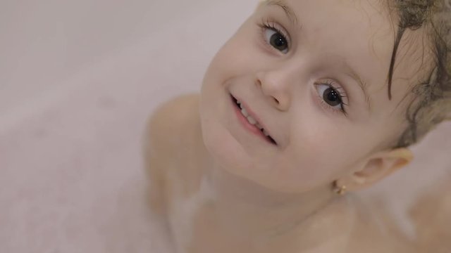 Attractive three years old girl  takes a bath. Wet hair with bath foam.  Cute blonde child. Brown eyes. Cute girl smiling. Pretty little child, 3-4 year old blonde girl in bathroom