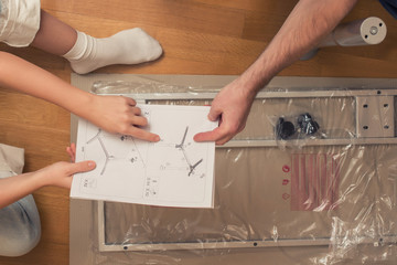 Man and woman assembling furniture  on wooden parquet using instruction for for self assembly