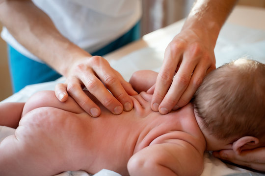 Picture from above of newborn baby and masseur hands.