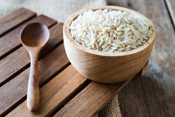 raw brown whole grain semi-milled rice in wood bowl with wood spoon on gunny sack cloth on wooden table